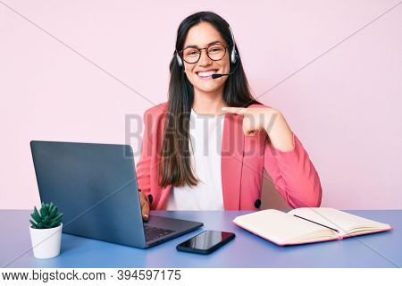 Young caucasian woman sitting at the desk wearing call center agent headset working using laptop pointing finger to one self smiling happy and proud 