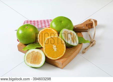 Still life of green grapefruits (sweetie, pomelit, oroblanco grapefruit) and halved orange with knife and tea towel on cutting board
