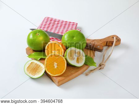 Still life of green grapefruits (sweetie, pomelit, oroblanco grapefruit) and halved orange with knife and tea towel on cutting board