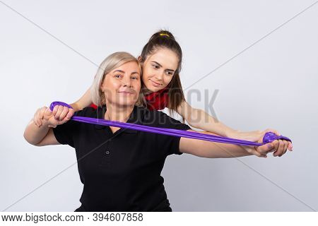 A Young Girl Fitness Instructor Helps An Older Woman To Do The Right Exercise. Photo On A White Back