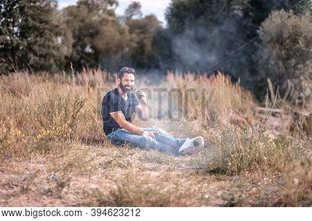Stylish Bearded Vape Man With Electronic Cigarette In Nature. Non-tobacco Smoking.