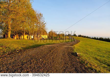 Autumn Hilly Landscape With Country Road At Sunset Time. Colorful Trees And Meadows Around Cottage U