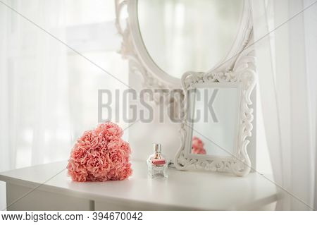 Pink Flowers On The Dressing Table In The White Bedroom. Flowers And Perfumes In A Bright Interior. 