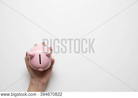 Womans Hand With Red Manicure Holds Money Piggy Bank On White Background. Flat Lay, Top View, Creati