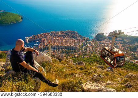 Wide Shot From The Top Of The Srd Mountain, Man Sitting On A Rock Observing The Area Around The City