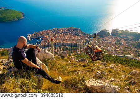 Wide Shot From The Top Of The Srd Mountain, Man Sitting On A Rock Observing The Area Around The City