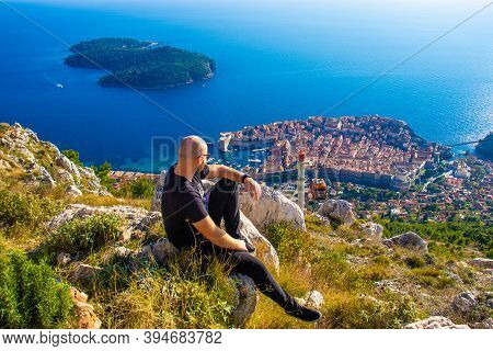 Wide Shot From The Top Of The Srd Mountain, Man Sitting On A Rock Observing The Area Around The City