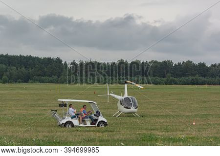 Belarus, Minsk - 07/25/2018: Electric Car And Two-seater Helicopter On The Green Field Of The Airfie