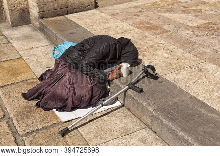 A Beggar Old Woman Lies On The Steps In Front Of The Entrance To The Church