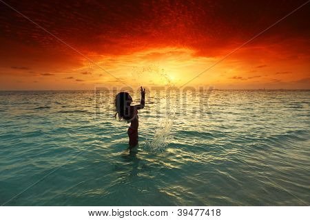 Vrolijke vrij jonge vrouw splashin in zee op zonsondergang