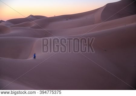 Unrecognizable Berber Man Walking On A Dreamy Desert At Twilight Of Dawn. Desert Dune Of Erg Chigaga