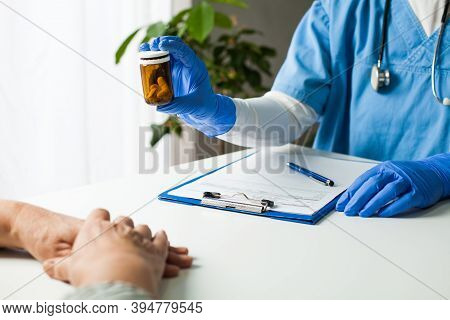 General Practitioner UK GP doctor holding bottle of prescription drugs,handing over to patient during medical check up,healthcare professional prescribing treatment therapy to elderly senior citizen