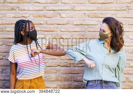 Multiethnic Young Women Wearing Masks Greeting At Each Other With Their Elbows