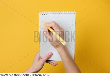 Female Hands Write With Pen In Notebook On Yellow Background. Girl's Diary. Pastel Color Trend. Top 