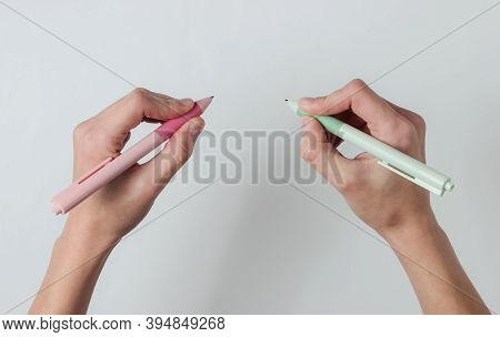 Ambidextr. Female Hands Hold Pens And Write On White Background. Top View. Studio Shot