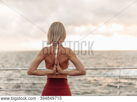 Yoga Practice At Sunrise. Young Female Yogi Making Namaste Behind The Back On Beach At Sunrise
