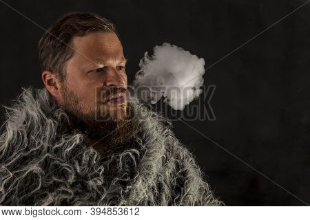 Solid Bearded Man Dressed In A Fur Mantle Exhaling Vapour
