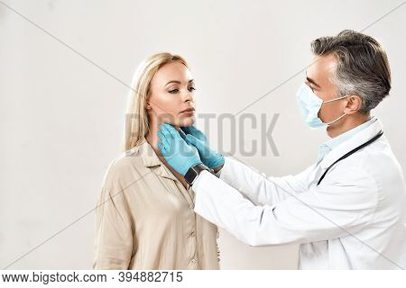 Sore Throat. Professional Mature Doctor In Medical Protective Mask Checking Thyroid Glands Of Young 