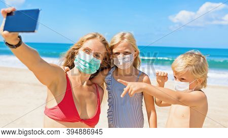 Funny Kids With Mother Taking Selfie Photo By Smartphone On Tropical Sea Beach. Rule To Wear Face Co