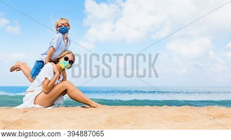 Mother, Child In Masks Have Fun On Sea Beach. New Rules To Wear Cloth Face Covering At Public Places