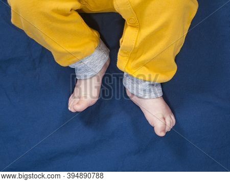 Baby Legs In Yellow Pants On Blue Background. Bare Feet
