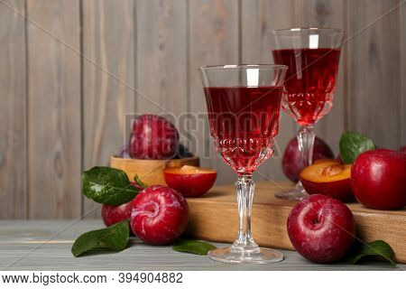Delicious Plum Liquor And Ripe Fruits On Grey Wooden Table, Space For Text. Homemade Strong Alcoholi