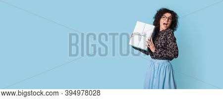 Curly Haired Woman Is Showing At Camera A Present Box Posing Happily Near Blue Free Space