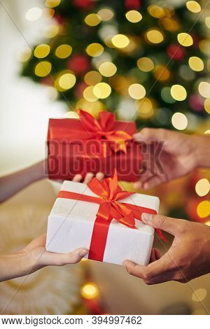 Hands Of Young People Giving Each Other Christmas Presents With Red Bows