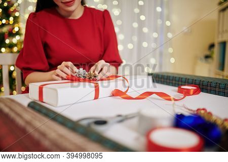 Cropped Image Of Young Woman In Red Dress Decorating Christmas Present With Pine Cone