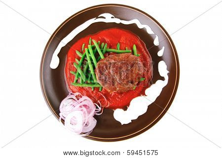 pork medallion served on tomato sauce with green peas on dark plate isolated on white background