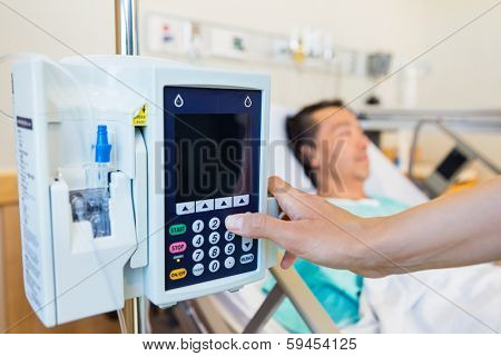 Closeup of nurse's hand operating IV machine while patient lying on bed in hospital