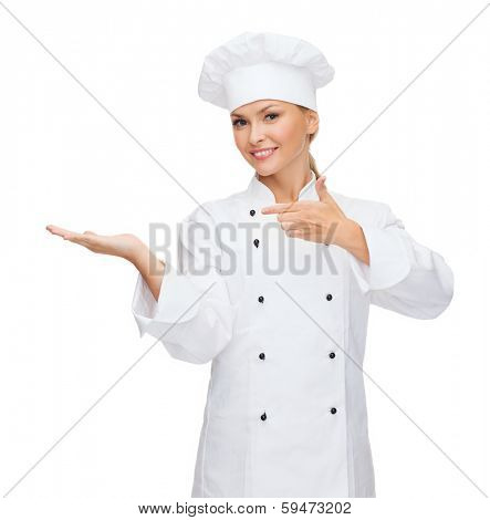 cooking, advertisement and food concept - smiling female chef, cook or baker holding something on palm of hand and pointing finger to it