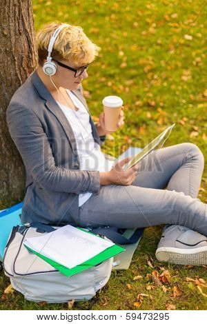education, technology and internet concept - smiling male student in eyeglasses with tablet pc, take away coffee and headphones outdoors