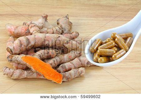 Fresh Turmeric rhizomes next to a spoon of Turmeric Capsules