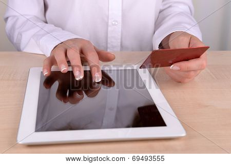 Female hands holding credit card and computer tablet on table close up