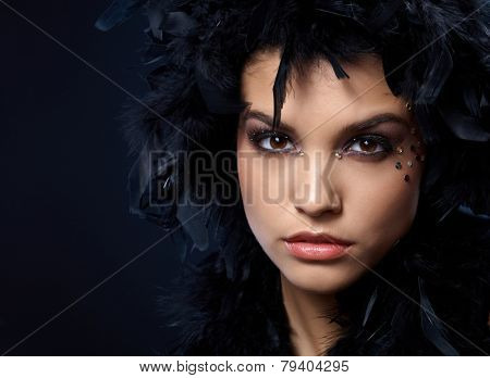 Extreme beauty with rhinestones makeup and wearing black feather boa on head.
