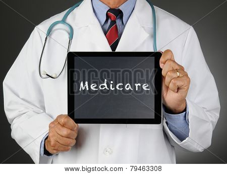 Closeup of a doctor holding a tablet computer with a chalkboard screen with the word Medicare. Man is unrecognizable.