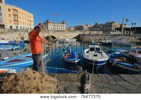 SIRACUSA, ITALY - JAN 03: fishing boats and fisherman in the darsena of Ortigia, Old Town of Siracusa in Sicily. The fisherman in foreground checks and arranges a fishing net. Shot in 2015 