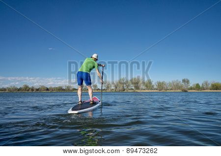 Senior male exercising on stand up paddling (SUP) board.. Early spring on calm lake in Fort Collins, Colorado..
