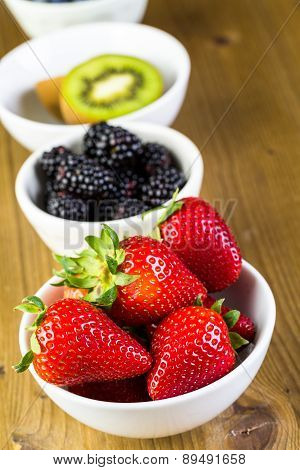 Organic fresh fruit in round bowls on wood table.