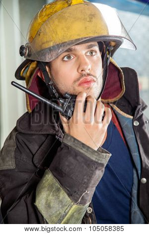 Confident male fireman looking away while using walkie talkie at fire station