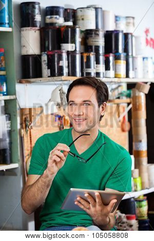 Thoughtful male worker holding eyeglasses and digital tablet in paper factory