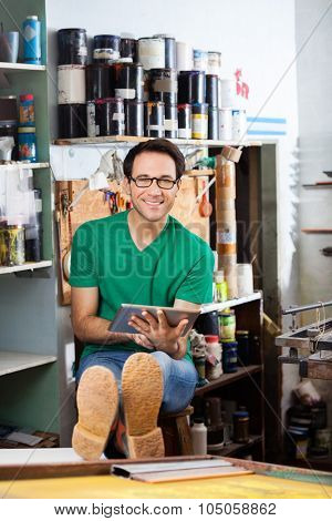 Portrait of confident worker using digital tablet while sitting in paper factory