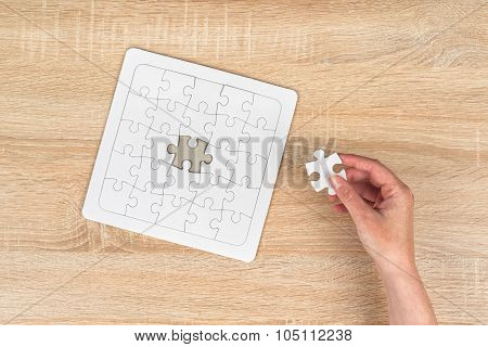 Female Hand Putting A Missing Piece Into Jigsaw Puzzle