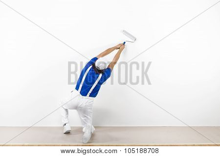 Squatting Painter With Paintroller On White Wall