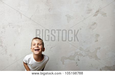 Little boy laughing at the camera. Cocrete wall on a background