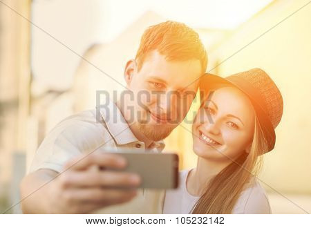 Touristic couple shooting on the modile phone selfy at the city streets under sunlight.