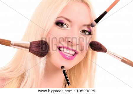 Giovane e bella donna bionda con molti pennelli su bianco e luminoso make-up