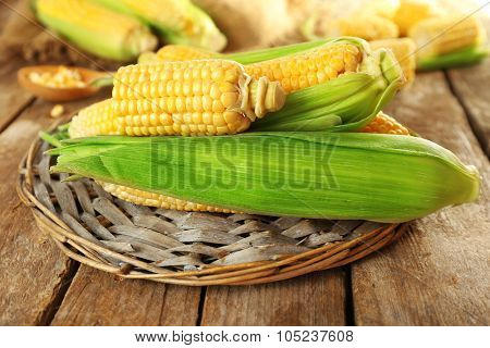 Fresh corn on cobs on wicker mat on wooden table, closeup