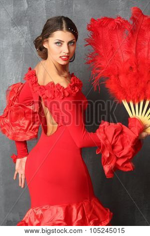Beautiful dancer in a red dress with a red plumage fan in hands stands half-turned